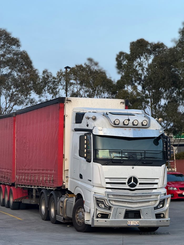 White and red semi truck parked outdoors at logistics hub, ready for transportation.